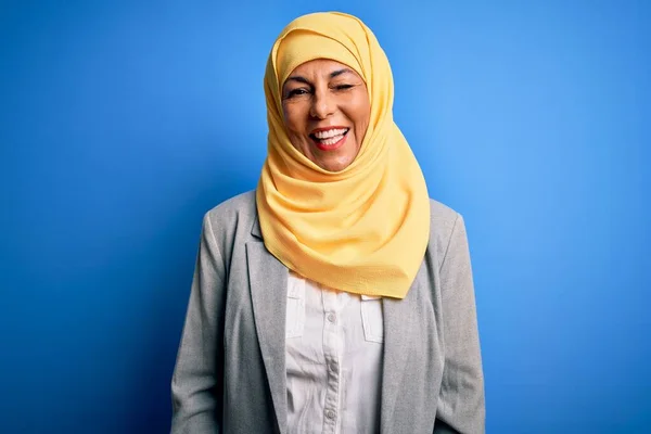 中世のブルネットビジネス女性身に着けていますムスリム伝統的なヒジャーブ上の青の背景ウィンク見ますでザ カメラとともにセクシー式 陽気で幸せな顔 — ストック写真