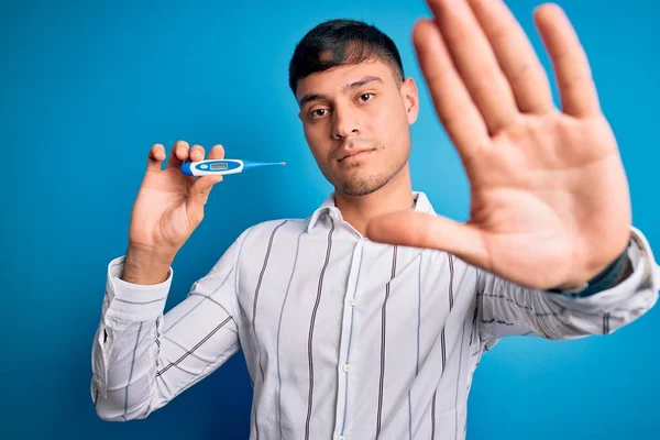 Junger Hispanischer Mann Hält Medizinisches Temperaturthermometer Über Blauem Isoliertem Hintergrund — Stockfoto