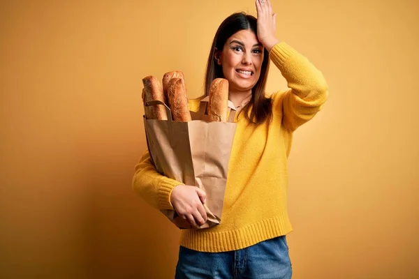 年轻美丽的女人抱着一袋黄色背景的新鲜健康的面包 手头上的错误让人吃惊 记住错误 记性差 — 图库照片
