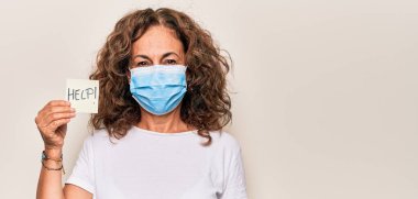 Coronavirus koruma maskesi takan orta yaşlı bir kadın elinde kağıt tutarak yardım istiyor. Pozitif ve mutlu görünüyor. Dişlerini gösteren bir gülümsemeyle ayakta duruyor.