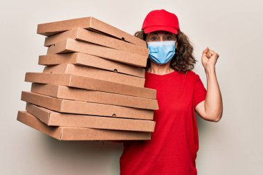 Coronavirus koruma maskesi takan orta yaşlı teslimatçı kadın elinde kartondan pizza kutuları tutarak gururla bağırıyor zaferi kutluyor ve başarıyı kollarını kaldırarak kutluyor.