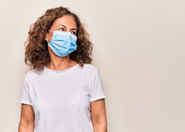 Orta yaşlı bir kadın covid-19 salgını için koronavirüs koruma maskesi takıyor. Taraf arıyor, rahat profil pozu veriyor, doğal bir yüzü ve kendine güvenen bir gülümsemesi var..