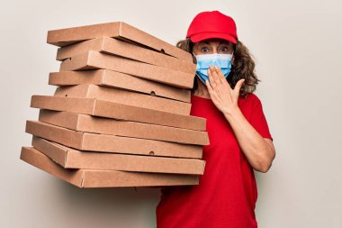 Coronavirus koruma maskesi takan orta yaşlı bir teslimatçı kadın ve elinde kartondan pizza kutuları var ağızlarını elle kapatıyor, şok geçiriyor ve hata yapmaktan korkuyor. Şaşırtıcı ifade.