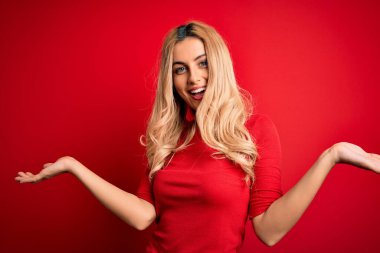 Güzel, sarışın bir kadın, gündelik tişört giyip kırmızı arka planda dikiliyor. Gülümsüyor, avuçlarını açıyor, sunuyor, reklam yapıyor, karşılaştırıyor ve dengede duruyor.