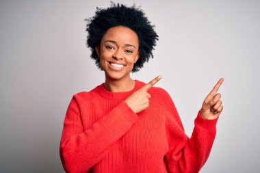 Kıvırcık saçlı, kırmızı süveter giyen, gülümseyen ve kameraya bakan iki eliyle ve parmaklarıyla yüzünü gösteren güzel Afrikalı bir afro kadın..