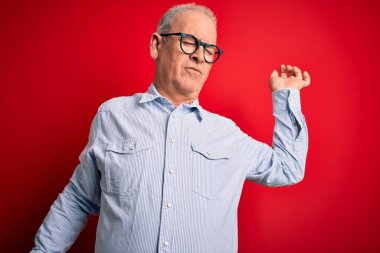 Orta yaşlı, yakışıklı, beyaz gömlekli ve gözlüklü, kırmızı arka planda gerinen, yorgun ve rahat, uykulu ve sabahın erken saatleri için esneyen bir adam.