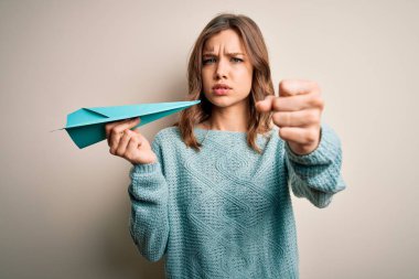 İş ve iletişim başarısı olarak elinde kağıt uçak tutan genç sarışın kız kızgınlıkla bağırıyor, deliriyor ve öfkeyle bağırıyor.
