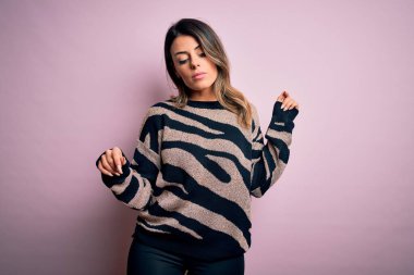 Moda kıyafetleri giyen genç ve güzel bir kadın. Manken, sokak tarzı giyiniyor. Pembe arka planda dikiliyor.