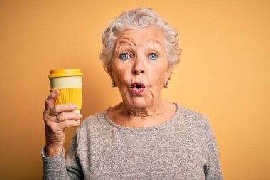 Üst düzey güzel bir kadın, sarı arka planda dikilmiş bir fincan kahve içiyor. Şaşırmış bir yüz ifadesinden korkuyor ve heyecanlanıyor.