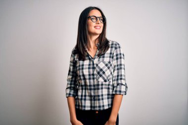 Mavi gözlü genç esmer kadın, beyaz arka planda günlük gömlek ve gözlük takıyor. Yüzünde gülümseme, doğal bir ifade ile diğer tarafa bakıyor. Kendinden emin gülen.