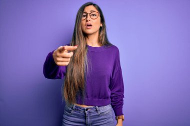 Genç, güzel, zeki, gözlüklü, mor renkli arka plan gözlüklü bir kadın. Kameraya kızgın ve sinirli olduğunu gösteriyor.