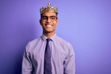 Genç ve yakışıklı Afro-Amerikalı adam mor arka planda kralın altın tacını takıyor ve yüzünde mutlu ve havalı bir gülümseme var. Şanslı kişi..