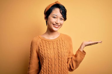 Sarı arka planda dikilip gülümseyen, eli kameraya bakan Asyalı güzel bir kız..