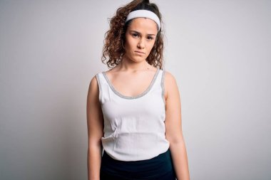 Kıvırcık saçlı güzel bir sporcu kadın izole edilmiş beyaz arka planda spor giysisi giyiyor ve yüzünde ciddi bir ifade var. Basit ve doğal bir şekilde kameraya bakıyorsun..