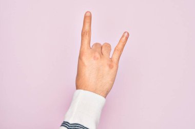 Kafkasyalı genç adam parmaklarını pembe arka planda gösteriyor rock 'n roll sembolü, müstehcen boynuzlar gösteriyor.