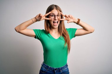 Genç, güzel, kızıl saçlı, yeşil tişörtlü ve gözlüklü bir kadın beyaz arka planda barış sembolü çiziyor.