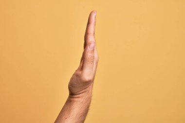 Kafkasyalı bir gencin elleri sarı arka planda parmaklarını gösteriyor. Uzanmış el hareketlerini gösteriyor, itiyor ve duruyor.