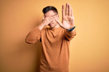 Gözlük takan yakışıklı beyaz bir adam ve sarı arka planda gelişigüzel bir süveter giyiyor gözleri ellerle örtüyor ve üzgün ve korku ifadeleriyle jest yapmayı kesiyor. Utanç verici ve olumsuz bir kavram..