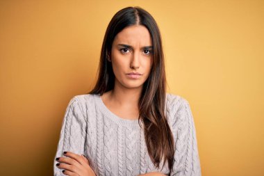 Sarı arka plan üzerine beyaz süveter giyen genç, güzel esmer kadın şüpheci ve gergin, yüzünde çapraz kollu tasvip etmeyen ifade. Negatif kişi.