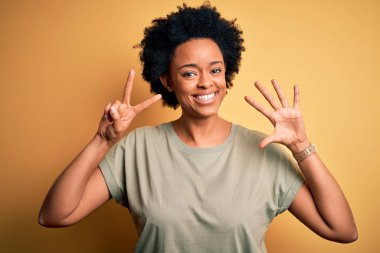 Kıvırcık saçlı, gündelik tişörtlü, genç ve güzel Afro-Amerikan kadın yedi numaralı parmaklarını gösterirken kendinden emin ve mutlu bir şekilde gülümsüyor..