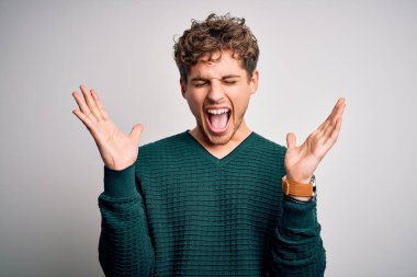 Sarışın, kıvırcık saçlı, yeşil süveter giyen, beyaz arka planda çılgın ve çılgın bir başarıyı kolları havada ve gözleri kapalı, heyecanlı bir şekilde kutlayan genç bir adam. Kazanan konsept