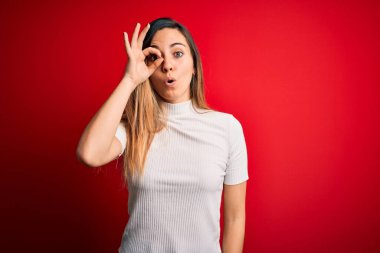 Kırmızı arka planda sıradan beyaz tişörtler giyen, mavi gözlü güzel sarışın kadın şaşırmış yüz ifadesiyle şaşırmış, parmaklarından bakan bir jest yapıyor. İnançsız ifade.