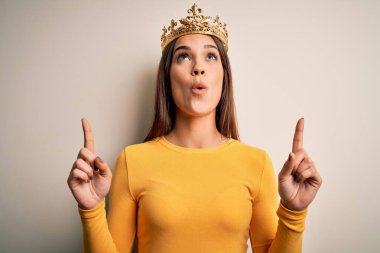 Beyaz arka planda altın kraliçe tacı takan genç, güzel esmer kadın şaşırmış ve şaşırmıştı. Parmaklarıyla işaret edip kollarını kaldırmıştı..