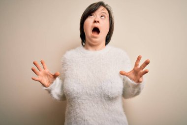 Genç Down sendromlu kadın izole arka planda duruyor çılgın ve kızgın bir şekilde bağırıyor ve agresif bir ifade ve kollarla bağırıyor. Hayal kırıklığı konsepti.