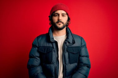 Sakallı, sıradan bir ceket giyen, kırmızı arka planda yün şapkalı, yüzünde ciddi bir ifade olan yakışıklı bir genç. Basit ve doğal bir şekilde kameraya bakıyorsun..