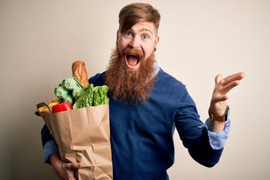 Kızıl saçlı, sakallı, süper marketten taze yiyecekler alan mutlu ve heyecanlı bir İrlandalı adam zaferi büyük bir gülümsemeyle ve el kaldırarak kutluyor.