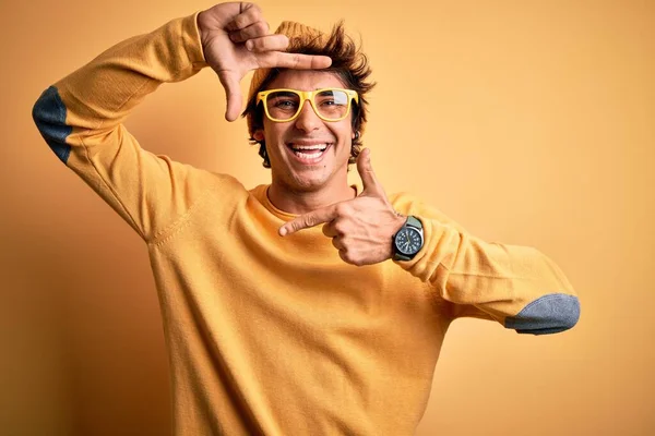 年轻英俊的男人穿着休闲装 戴着眼镜 戴在孤立的黄色背景上 微笑着 用双手和手指做着快乐的相框 创意和摄影概念 — 图库照片