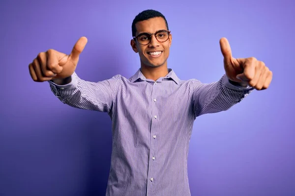 줄무늬 셔츠와 안경을 착용하고 보라색 위에서 손으로 긍정적 행동을 승인하는 — 스톡 사진