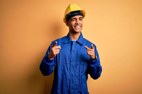 青の制服とセキュリティヘルメットを着ている若いハンサムなアフリカ系アメリカ人労働者の男性は 幸せで面白い顔をしてカメラに指を指している 良いエネルギーと振動 — ストック写真