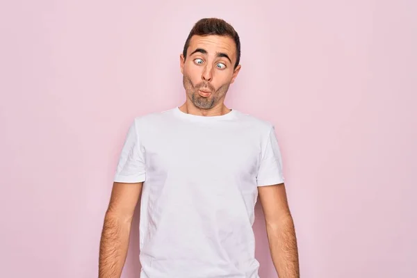 英俊的蓝眼睛男子穿着休闲的白色T恤 站在粉色背景之上 用嘴唇 疯狂和滑稽的姿势做鱼脸 有趣的表达方式 — 图库照片