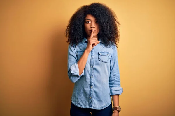 年轻美丽的非洲裔美国女人 有着非洲式的头发 站在黄色孤立的背景上 要求保持安静 手指放在嘴唇上 沉默和秘密概念 — 图库照片