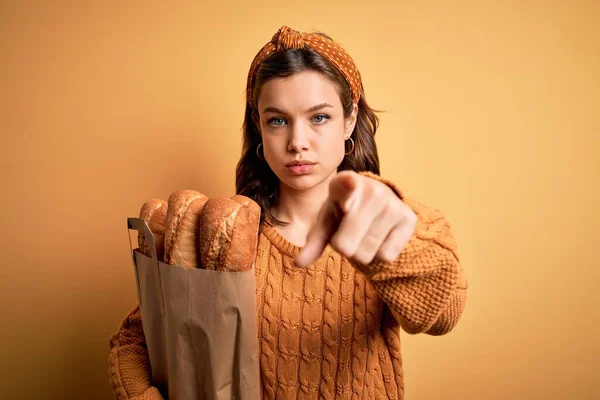年轻的金发姑娘拿着装有新鲜面包的超市纸袋 黄色背景 手指指向相机和你 正面是积极自信的手势 — 图库照片