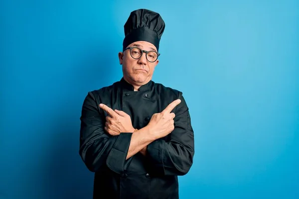 Middle age handsome grey-haired chef man wearing cooker uniform and hat Pointing to both sides with fingers, different direction disagree