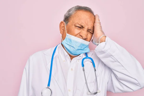 Senior hoary doctor man wearing medical mask and stethoscope over pink background stressed with hand on head, shocked with shame and surprise face, angry and frustrated. Fear and upset for mistake.