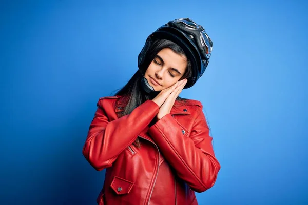 Young beautiful brunette motorcycliste woman wearing motorcycle helmet and jacket sleeping tired dreaming and posing with hands together while smiling with closed eyes.