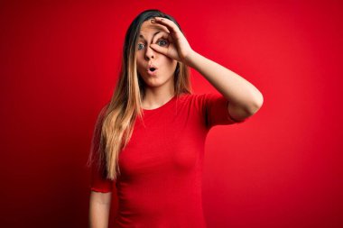 Kırmızı arka planda sıradan tişörtler giyen, mavi gözlü genç, güzel sarışın kadın şaşırmış yüz ifadesiyle şaşırmış, parmaklarından bakan bir jest yapıyor. İnançsız ifade.
