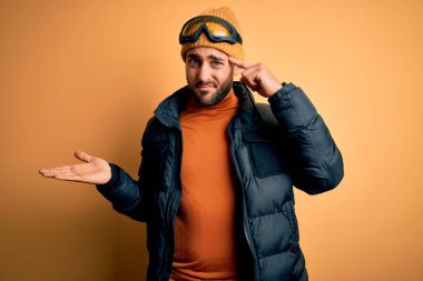 Kar giysileri ve kayak gözlüğü takan sakallı genç yakışıklı kayakçı, avuç içi açık, fotokopi alanı gösteren ve alnını göstererek kafasını karıştırıyor. Bunu bir düşün..