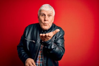 Kıdemli yakışıklı, beyaz gömlekli ve ceketli adam izole edilmiş kırmızı arka planda kameraya bakıyor ve havada bir öpücük savuruyor. Güzel ve seksi. Aşk ifadesi.