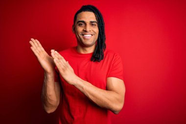 Genç, Afro-Amerikan Afrikalı, rastalı kırmızı tişörtlü, mutlu ve neşeli, gururlu elleri alkışlayan genç bir adam.