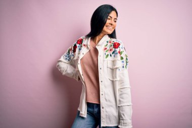 Moda kıyafetleri giyen genç ve güzel bir kadın. Manken, sokak tarzı giyiniyor. Pembe arka planda dikiliyor.