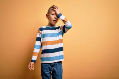 Küçük, beyaz, mavi gözlü, sarı arka plan üzerine renkli çizgili tişört giyen, hata sonucu el ele tutuşan genç bir çocuk. Hatayı hatırla. Unuttum, kötü hafıza konsepti.