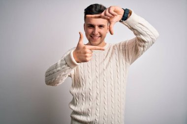 Beyaz izole edilmiş arka planda günlük kazak giyen yakışıklı beyaz bir adam gülümseyerek elleri ve parmakları gülen yüzlü bir çerçeve yapıyor. Yaratıcılık ve fotoğrafçılık kavramı.