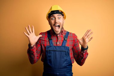 Sarı arka plan üzerinde inşaat üniforması ve güvenlik kaskı takan genç müteahhit çılgın ve başarıyı kollarını kaldırıp heyecanla haykırarak kutluyor. Kazanan konsept