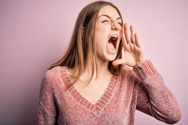 Genç, güzel, kızıl saçlı bir kadın pembe arka plan üzerine günlük süveter giyip el ele bağırıyor ve çığlık çığlığa bağırıyordu. İletişim konsepti.