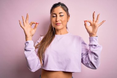 Pembe izole edilmiş arka plan üzerine kazak giyen genç ve güzel bir kadın rahatla ve parmaklarıyla meditasyon hareketi yaparken gözleri kapalı gülümse. Yoga konsepti.