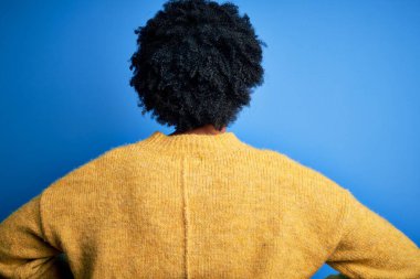 Kıvırcık saçlı, sarı kazaklı, güzel Afro-Amerikan kadın geriye doğru bakıyor kolları vücudunda.